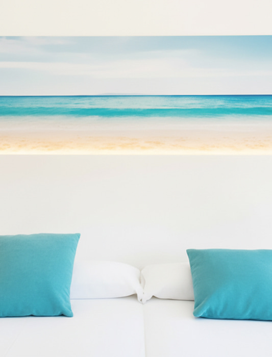 Detalle Habitación Detalle de la cabecera de la cama, con cojines de color azul y un cuadro de estilo mediterráneo