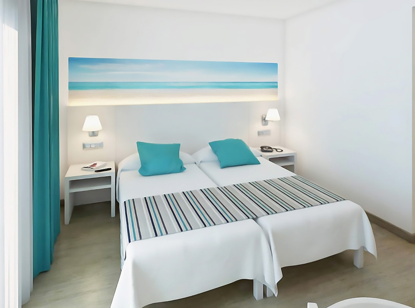 Habitación Doble con Balcón_Camas Dos camas individuales juntas, con sábanas blancas, cojines azul turquesa y un cabecero decorado con un cuadro de inspiración mediterránea.